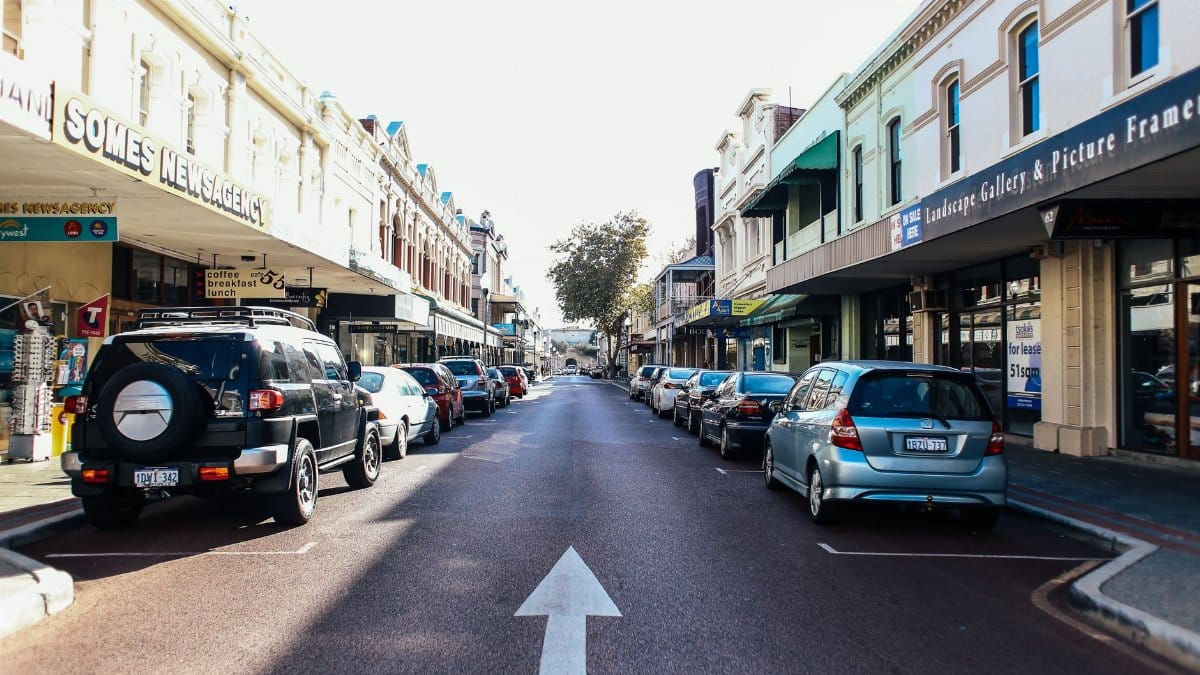 Vibrant city street with parked cars and local shops on a sunny day.