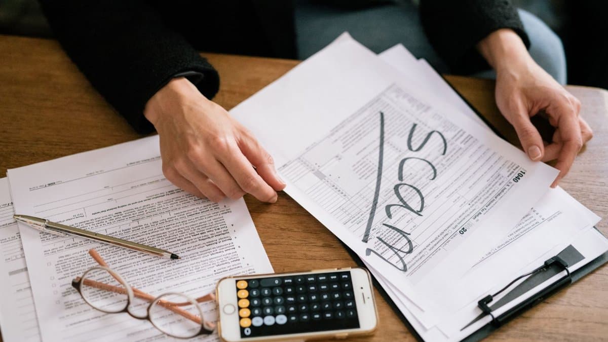 Hands of a person examining tax forms labeled as scam with calculator and papers.