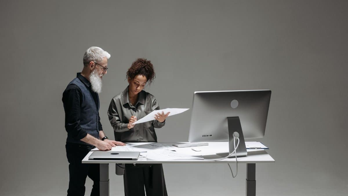 Professional team discussing over documents at a modern office setup with large monitor.