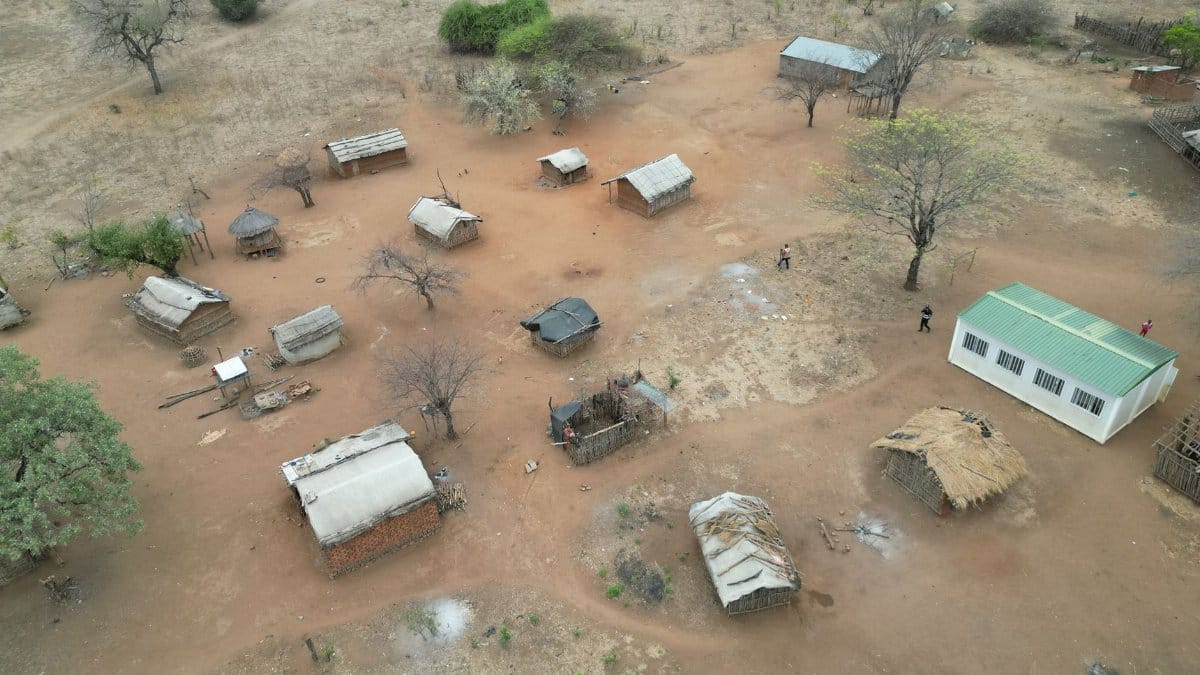 An aerial shot showcasing a rural African village with traditional huts and a community building.