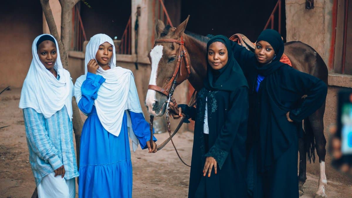 Four Nigerian women in traditional attire with a horse outside a stable, showcasing cultural heritage.