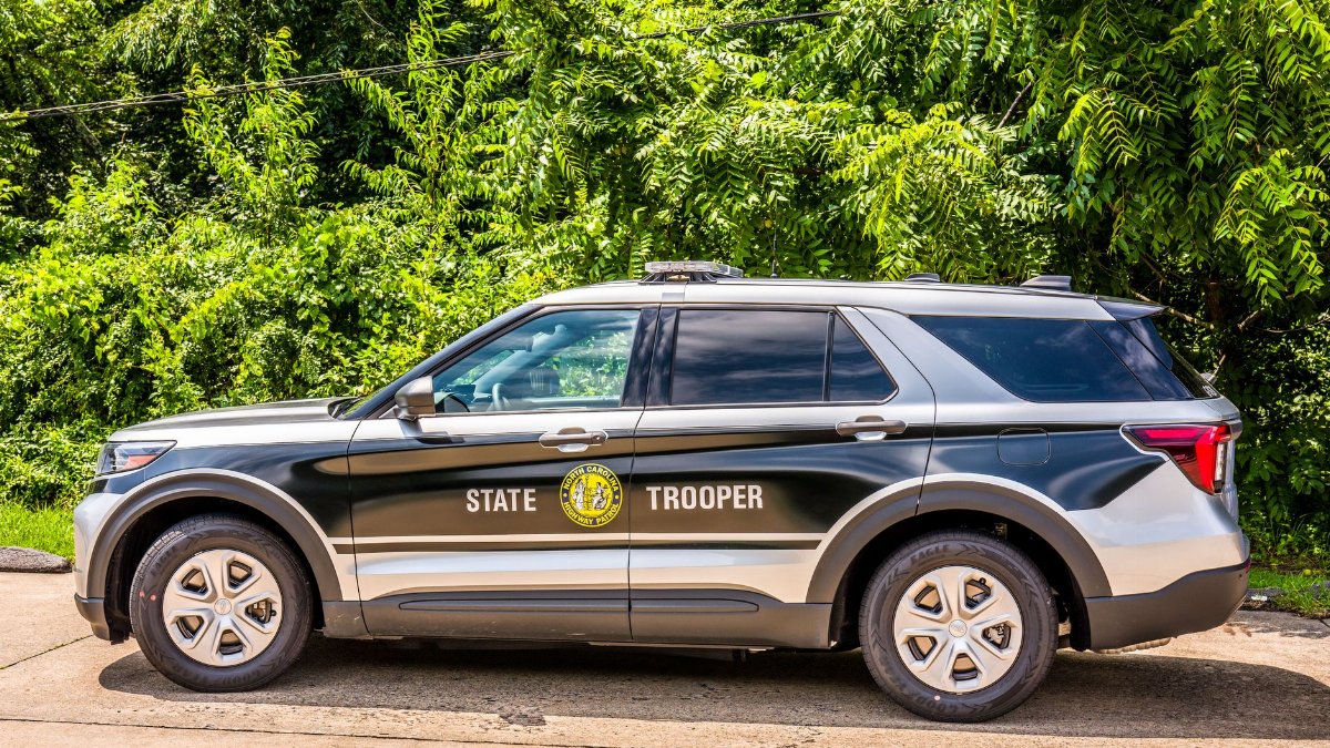 State trooper SUV parked on a sunny day with lush greenery in the background.