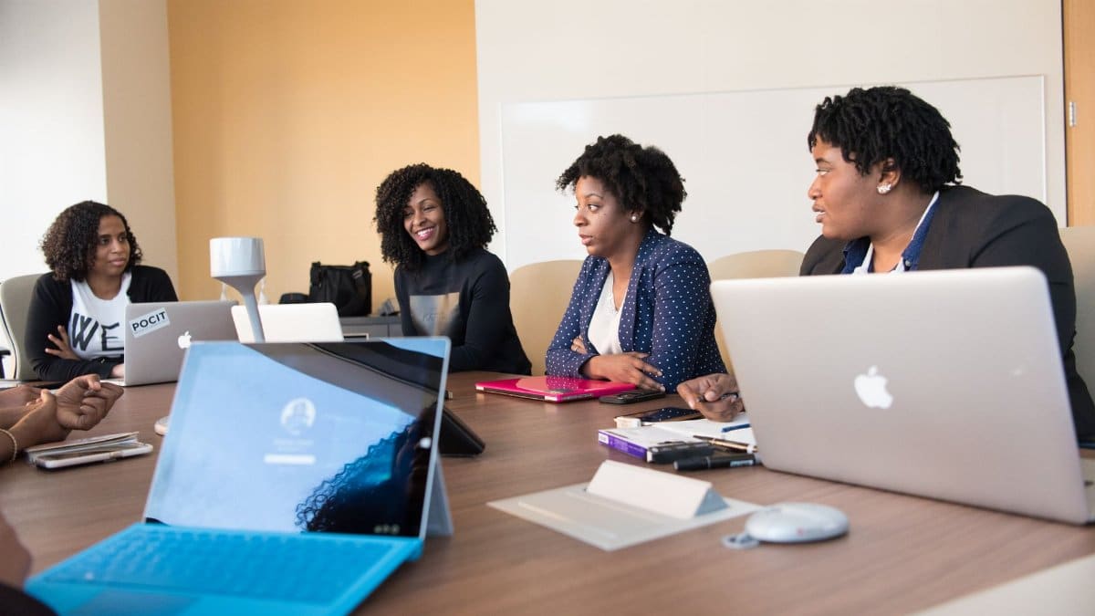 Black women collaborating with laptops in an office meeting, enhancing teamwork and technology.