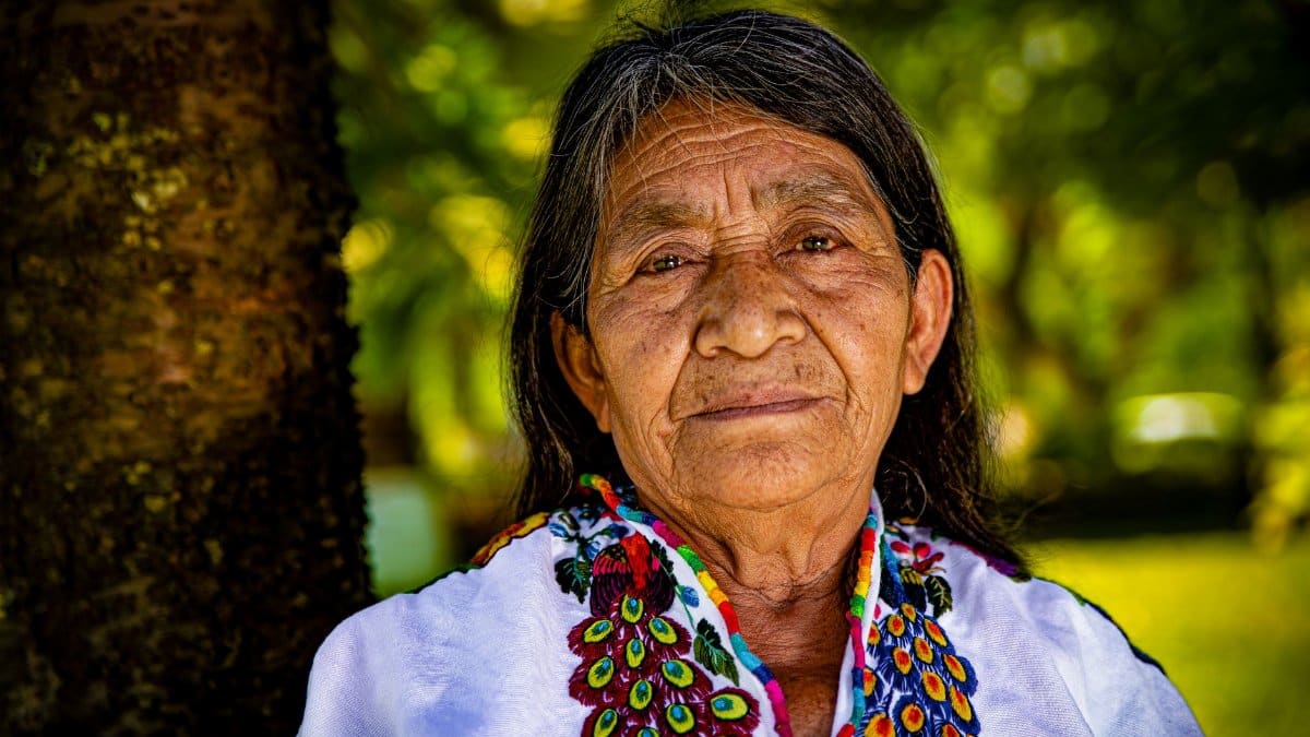 Elderly indigenous woman in colorful traditional attire, outdoors, close-up.