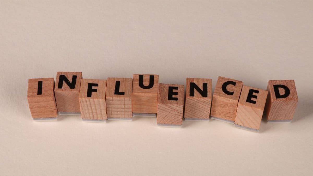 Wooden blocks with letters spelling 'Influenced' arranged on a beige surface.