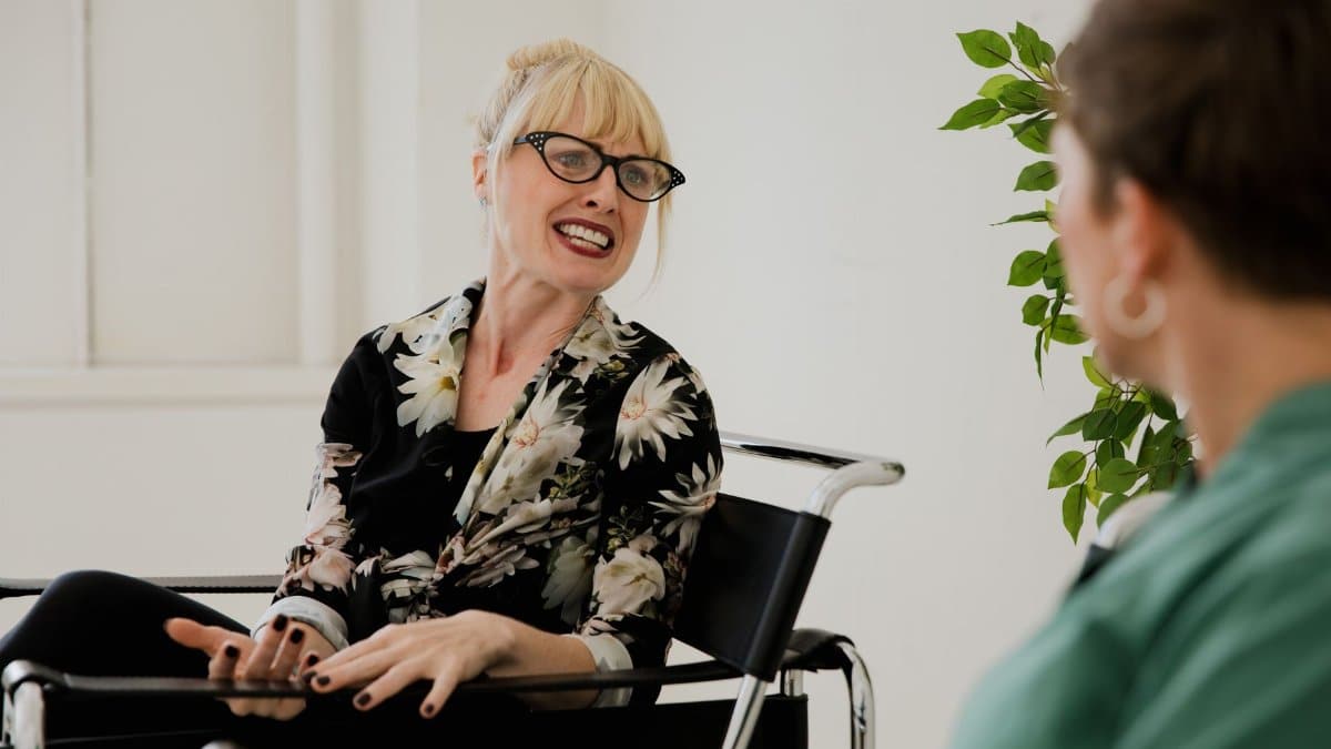 Blonde woman with glasses actively talking during an indoor counseling session.