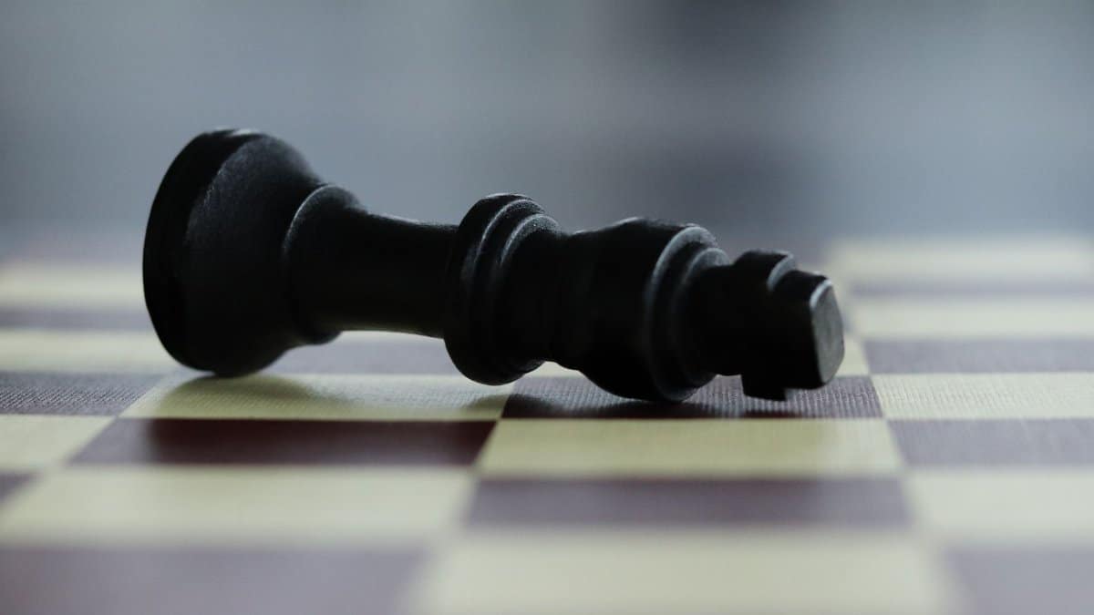 Close-up of a chess queen lying on a chessboard, symbolizing defeat.