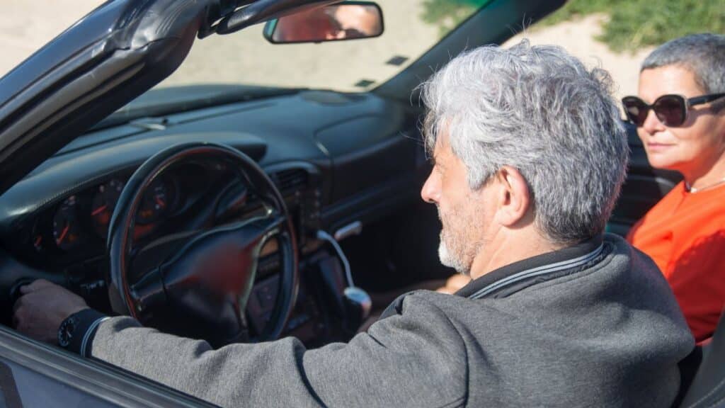 Senior couple enjoying a sunny drive in a convertible through scenic Portugal.