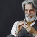 Stylish senior man with gray hair and cigar lighting a lighter, wearing eyeglasses, vest, and polka dot scarf.