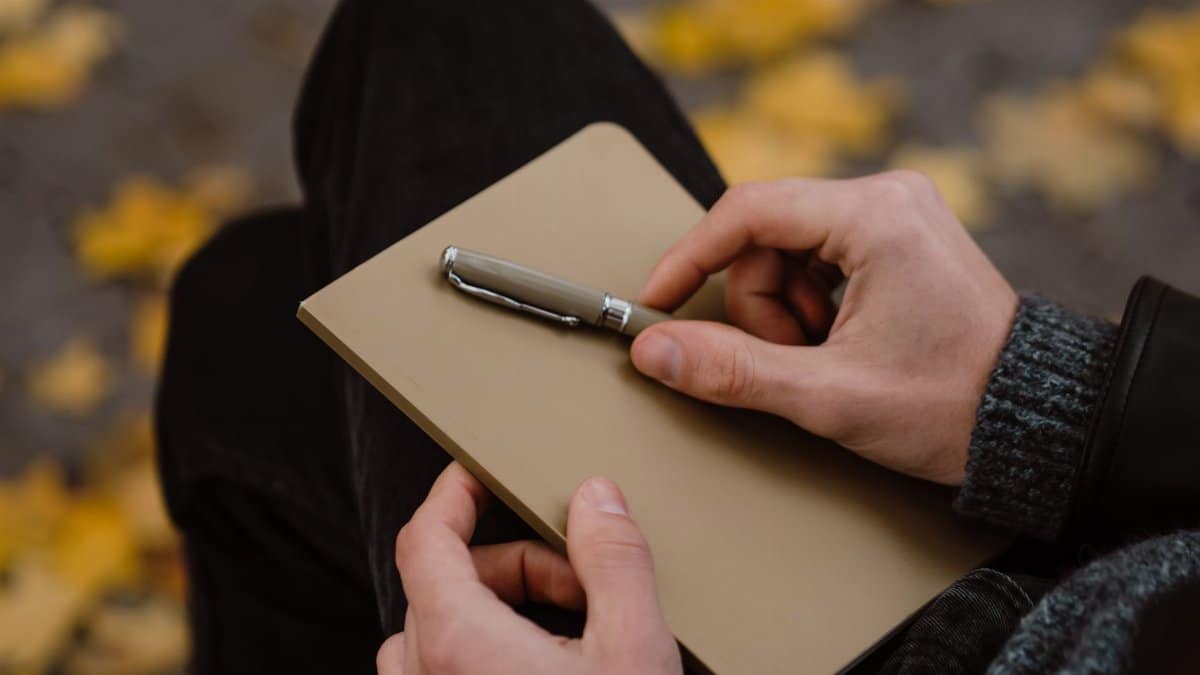 Hands holding a notebook and pen in a cozy autumnal setting. Perfect for journaling themes.
