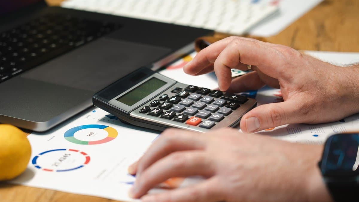 A person analyzing financial data using a calculator and laptop on a desk.