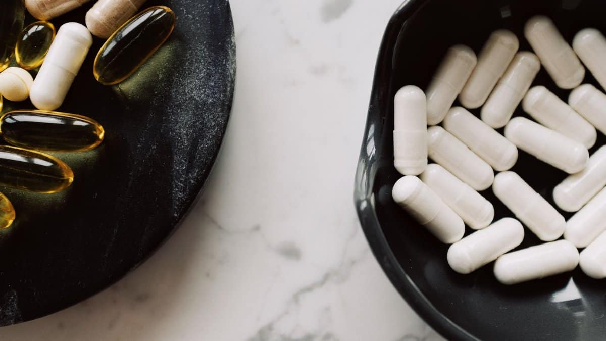 Assorted capsules and pills on black plates, featuring vitamins and supplements.