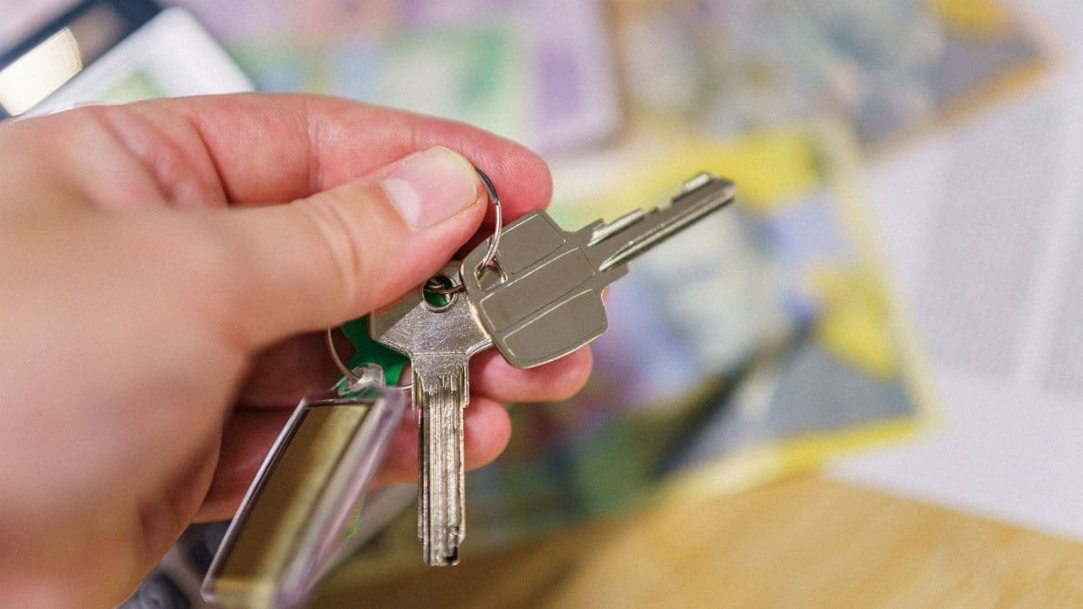 Close-up of keys in hand representing property ownership with blurred financial documents in the background.