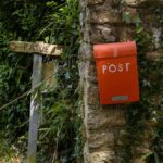 Charming red post box on an ivy-covered stone wall in Brittany, France, near a rustic gate and greenery.