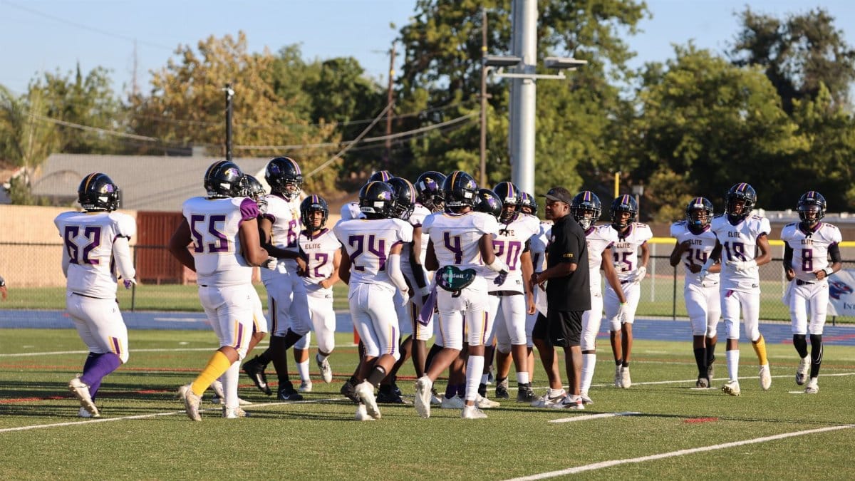 Youth American football team huddled on sunlit field during game. Players in sportswear discussing strategy.