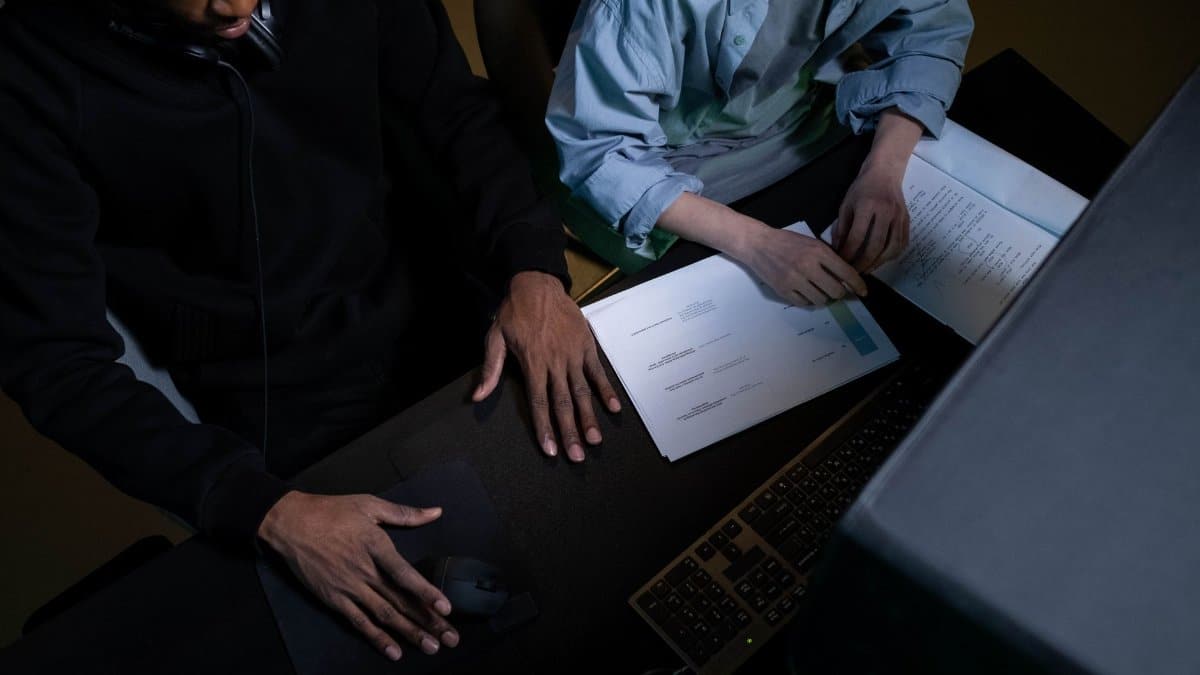 Two colleagues work over papers and a computer at a desk, collaborating effectively.