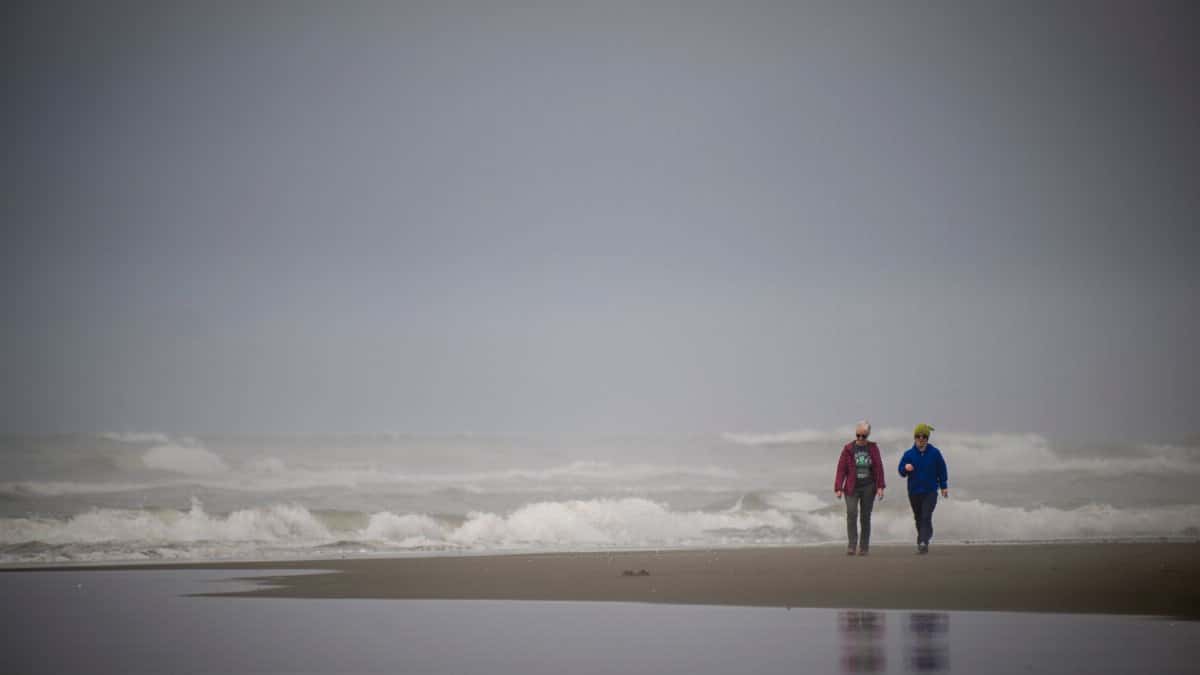 Two adults walking along Ocean Shores beach in Washington with waves crashing in the background.