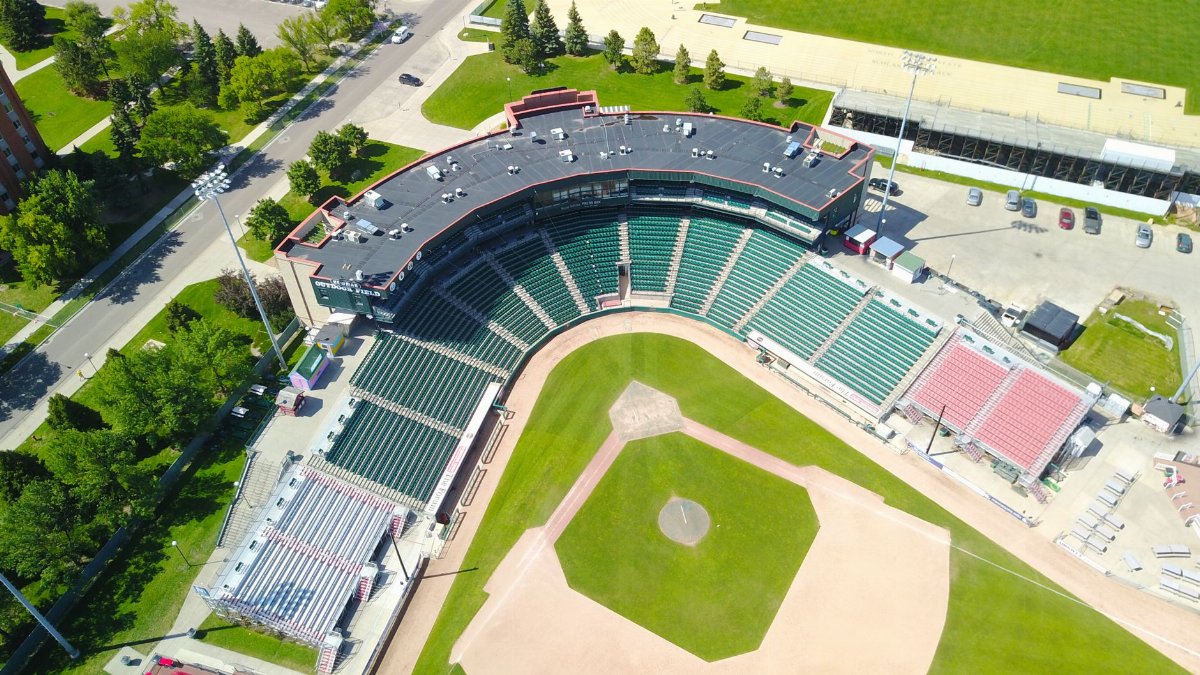 Drone shot of an empty baseball stadium surrounded by greenery under clear skies.