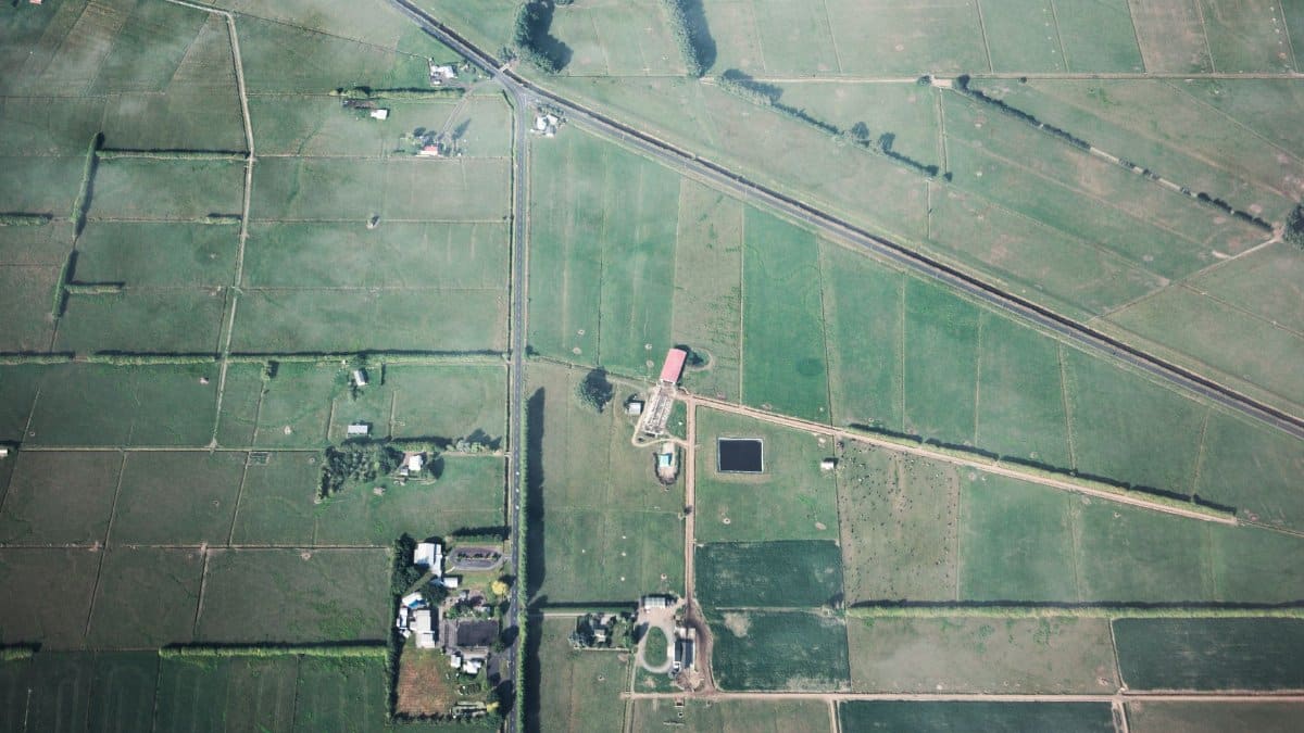 Aerial shot showcasing expansive green farmland with field boundaries and rural structures.