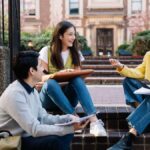 A group of college students sitting and discussing on university steps, engaging in lively conversation.
