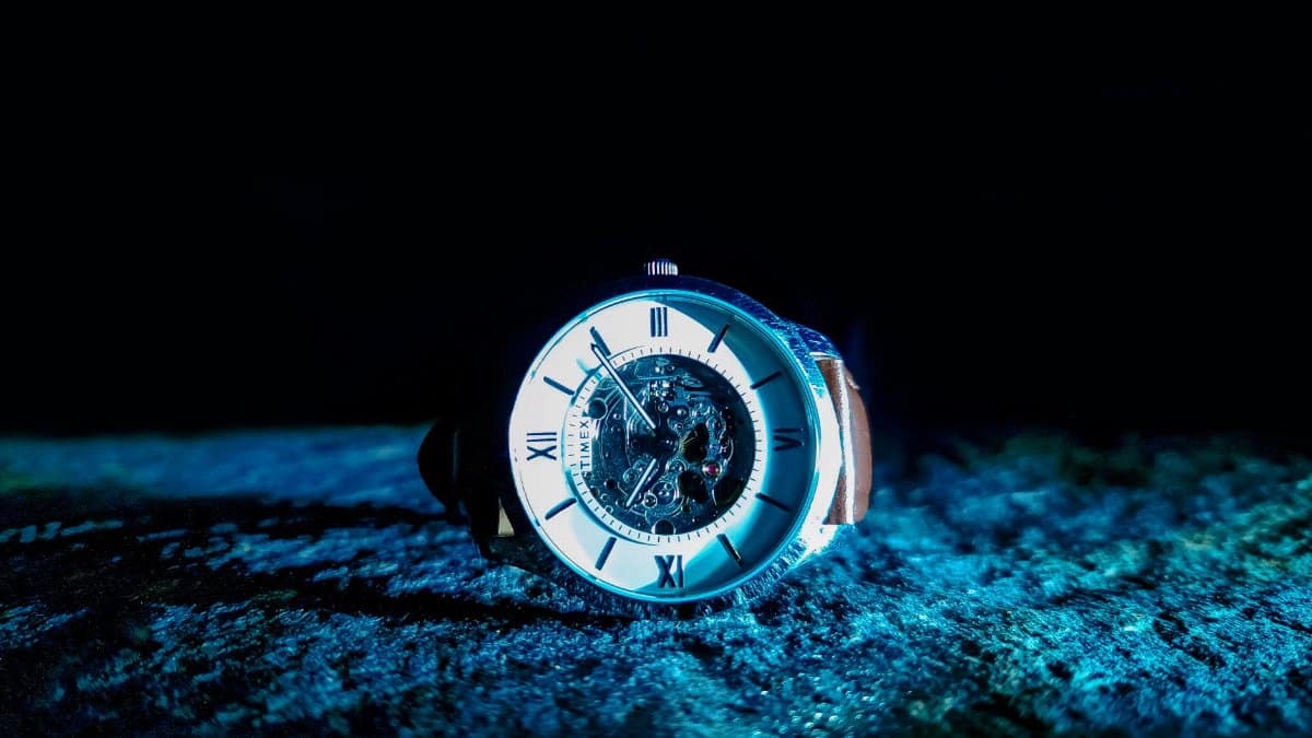 Close-up of a mechanical watch with Roman numerals, illuminated in dramatic lighting.