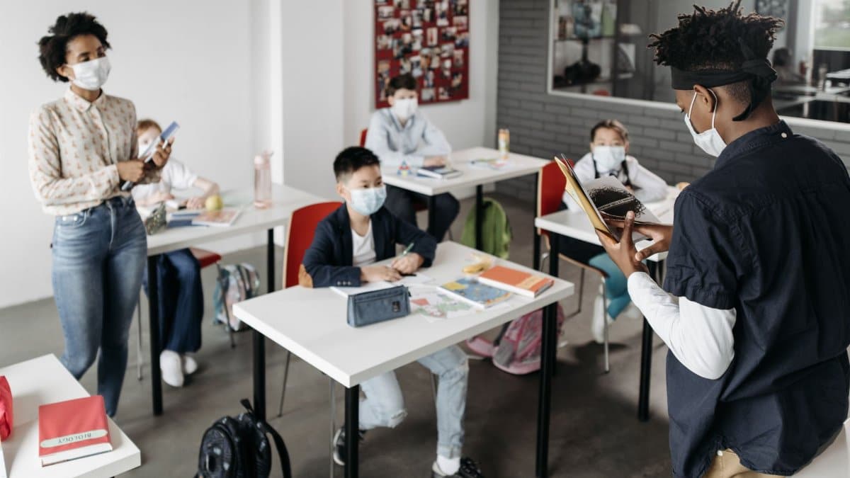 A diverse group of students and a teacher wearing masks in a classroom.