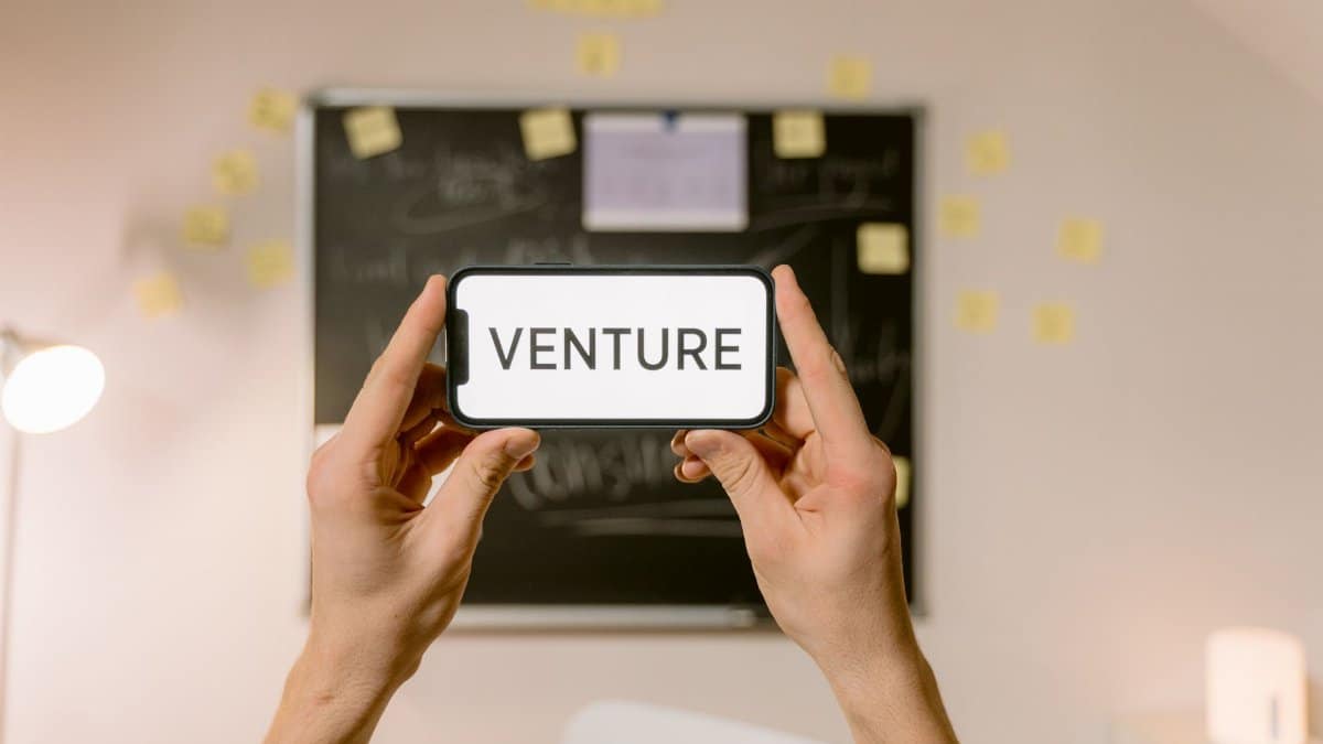 A smartphone displaying 'Venture' held by hands in an office setup. Ideal for business and startup themes.