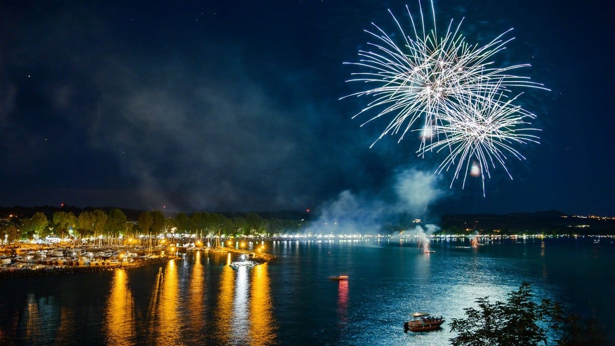 Dazzling fireworks light up the night sky over a serene lake, reflecting vivid colors in the water.