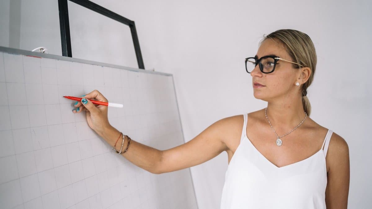 Confident female teacher explaining a concept on a whiteboard in a classroom setting.