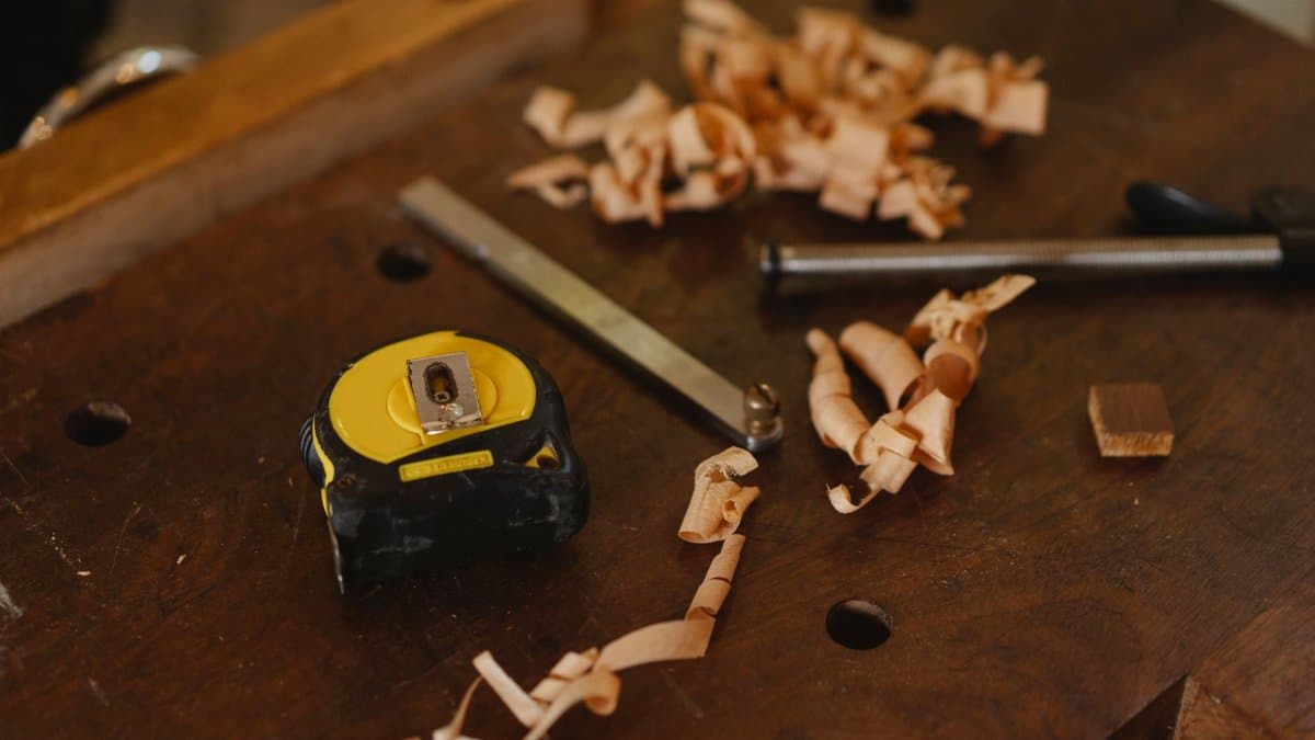 From above of tape measure near metal carpentry instruments with wooden shavings in workshop