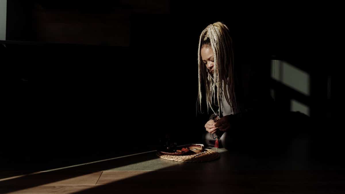 A woman with braided hair arranges a tray of sliced fruits in dim lighting, creating a serene ambiance.