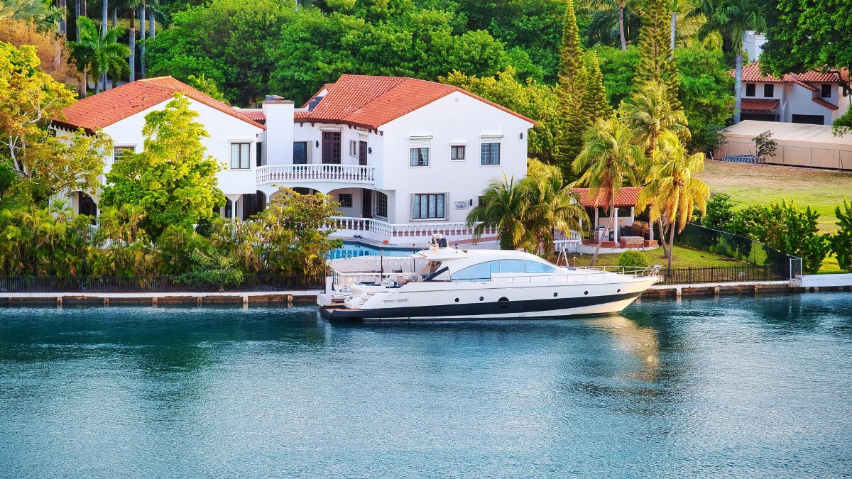 Elegant Miami luxury villa by the waterfront with a yacht docked nearby, unique architecture and tropical setting.