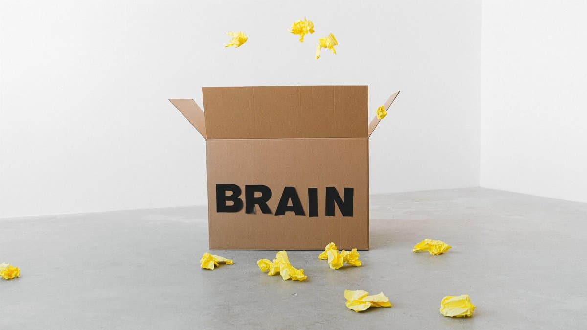 Crumpled yellow paper pieces on floor near carton box with Brain title on white background
