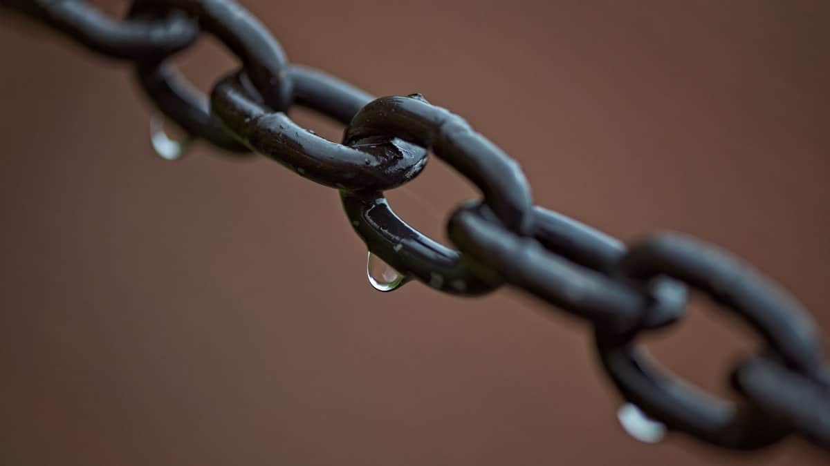 Macro shot of metal chain links with raindrops, showcasing texture and moisture.
