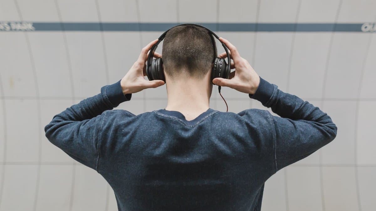 Man with headphones listening to music indoors, wearing long sleeves. Back view shot.