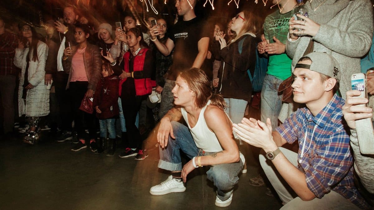 A lively group of diverse people gathered indoors, enjoying a vibrant live performance under dynamic lighting.
