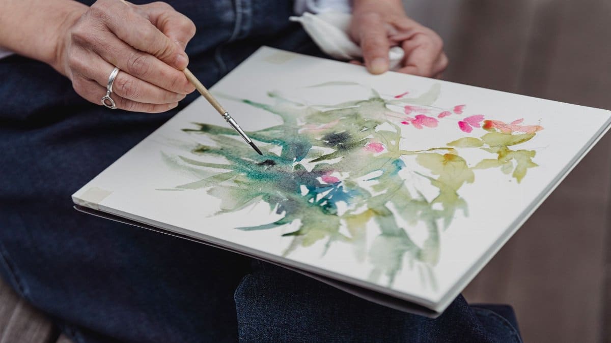 Close-up of an artist painting a botanical watercolor in a sketchbook, showcasing creative expression.