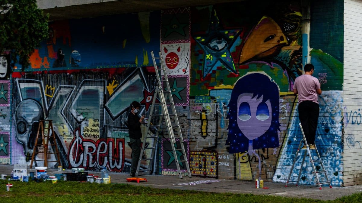Two artists painting a vibrant mural on a city wall, showcasing modern street art.
