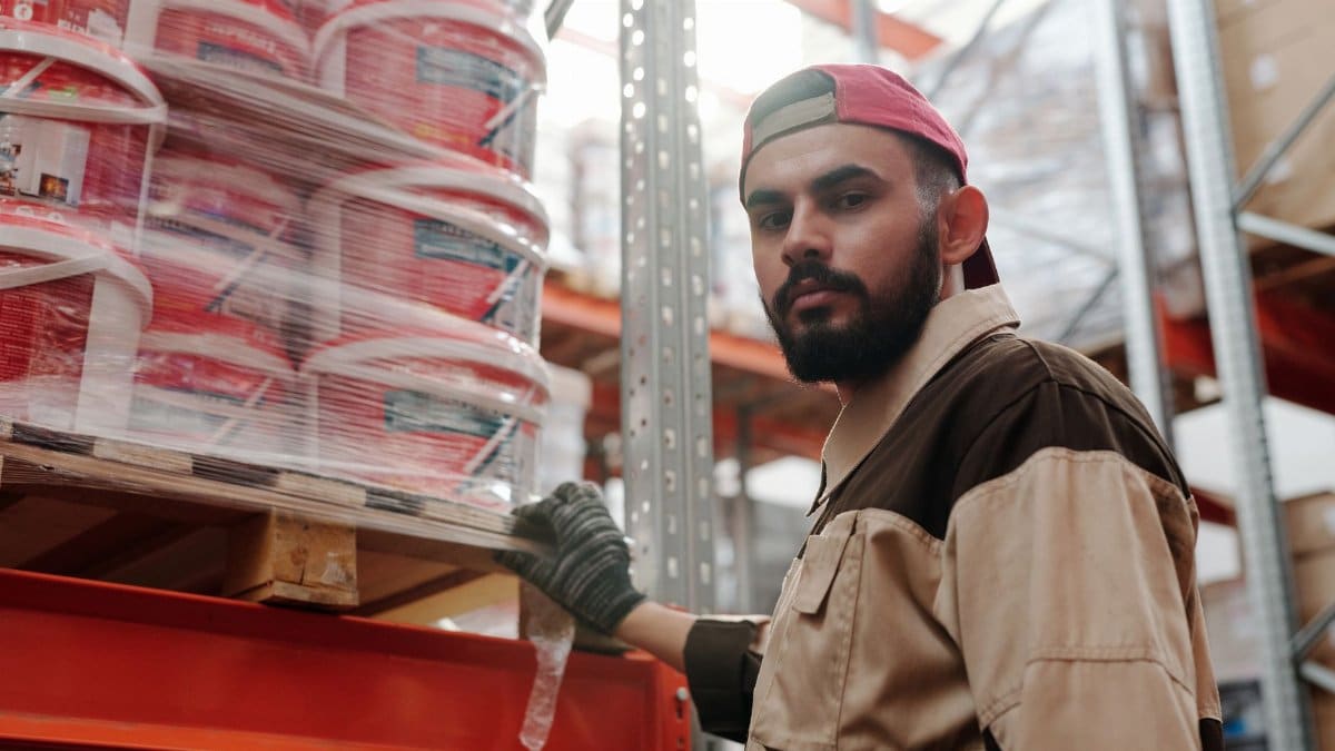 Portrait of a male warehouse worker standing next to stacked paint buckets indoors.