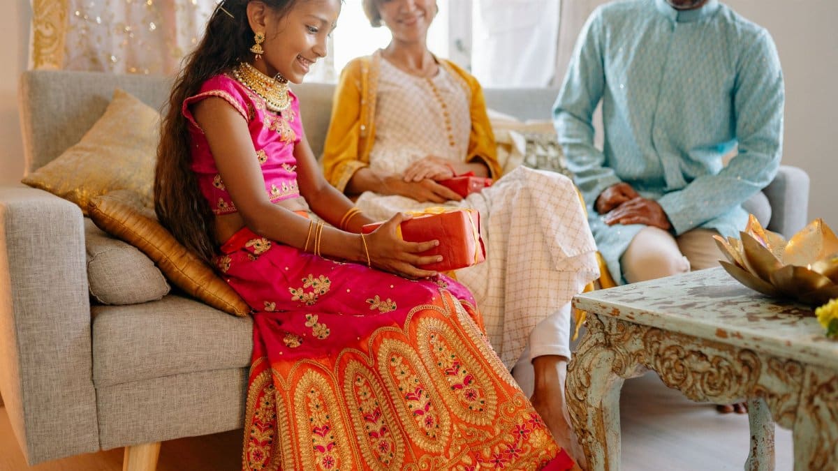 Smiling family celebrating Diwali with a child receiving a gift in traditional Indian clothing indoors.