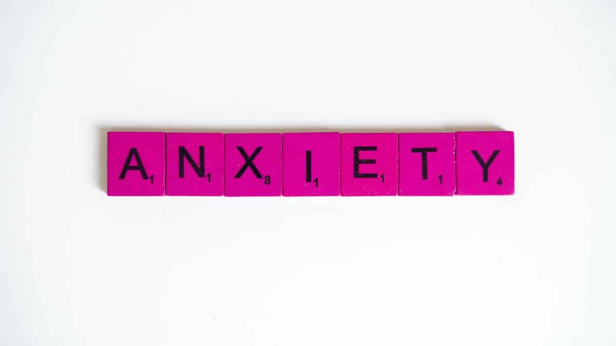 Pink Scrabble tiles spelling 'anxiety' on a white surface. Concept of mental health.