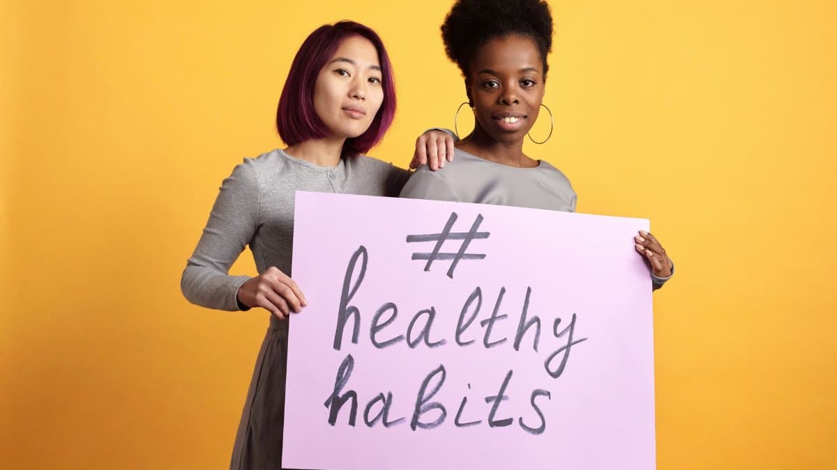 Two women holding a sign with '#healthy habits' on a vibrant yellow background.