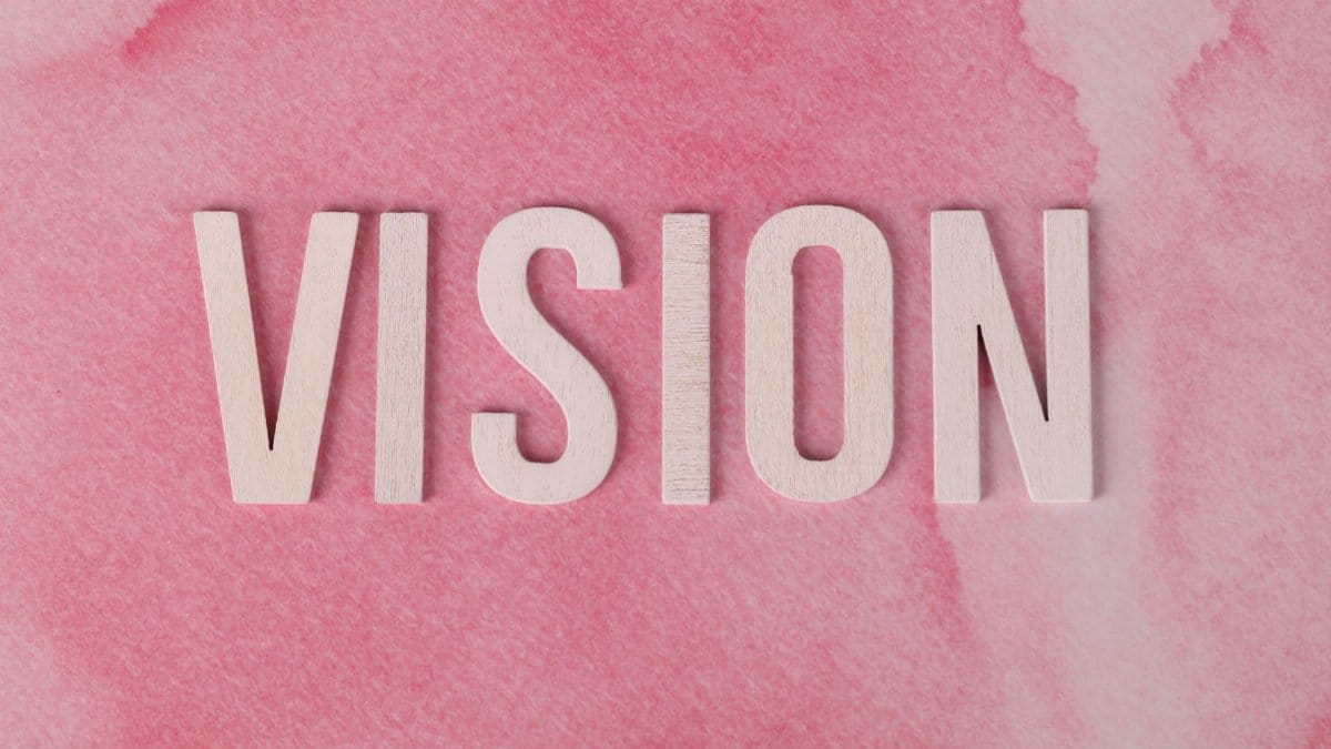 Wooden letters spelling 'VISION' on a textured pink watercolor background.