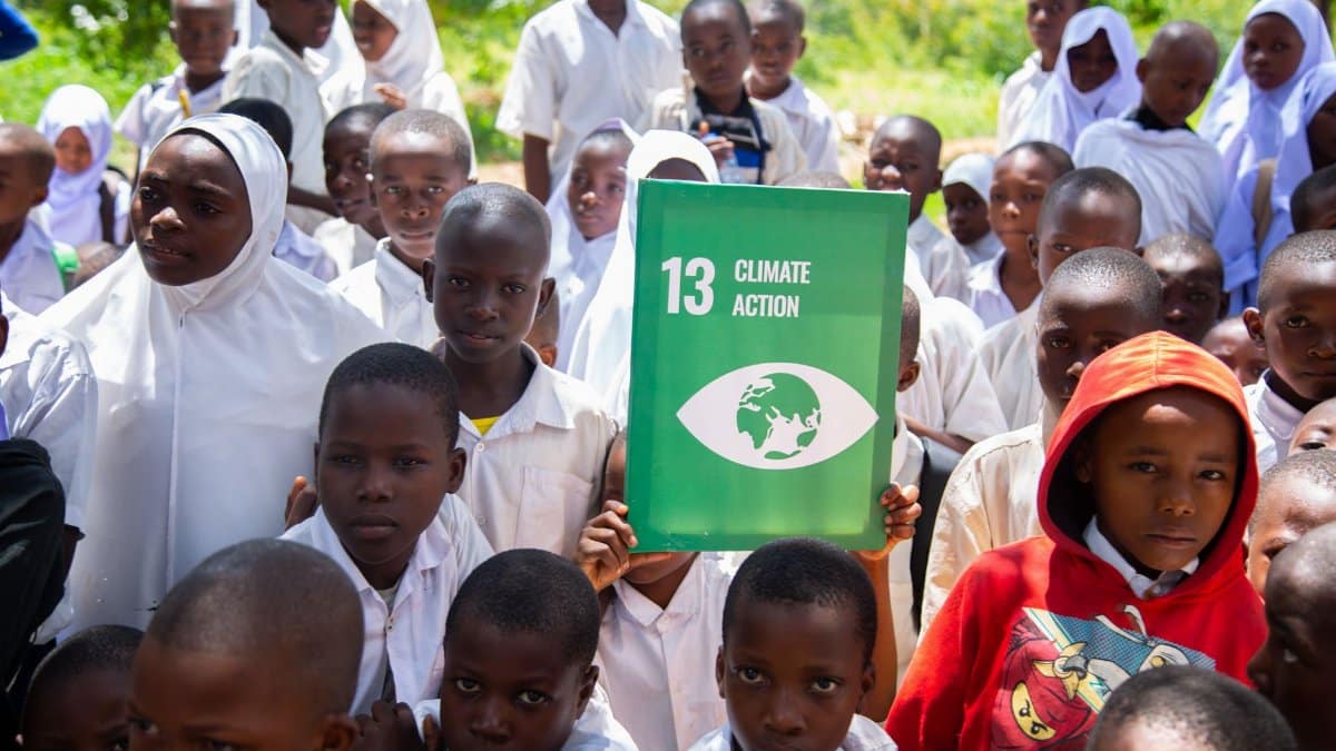 Group of students holding a Climate Action sign in outdoor environmental setting.