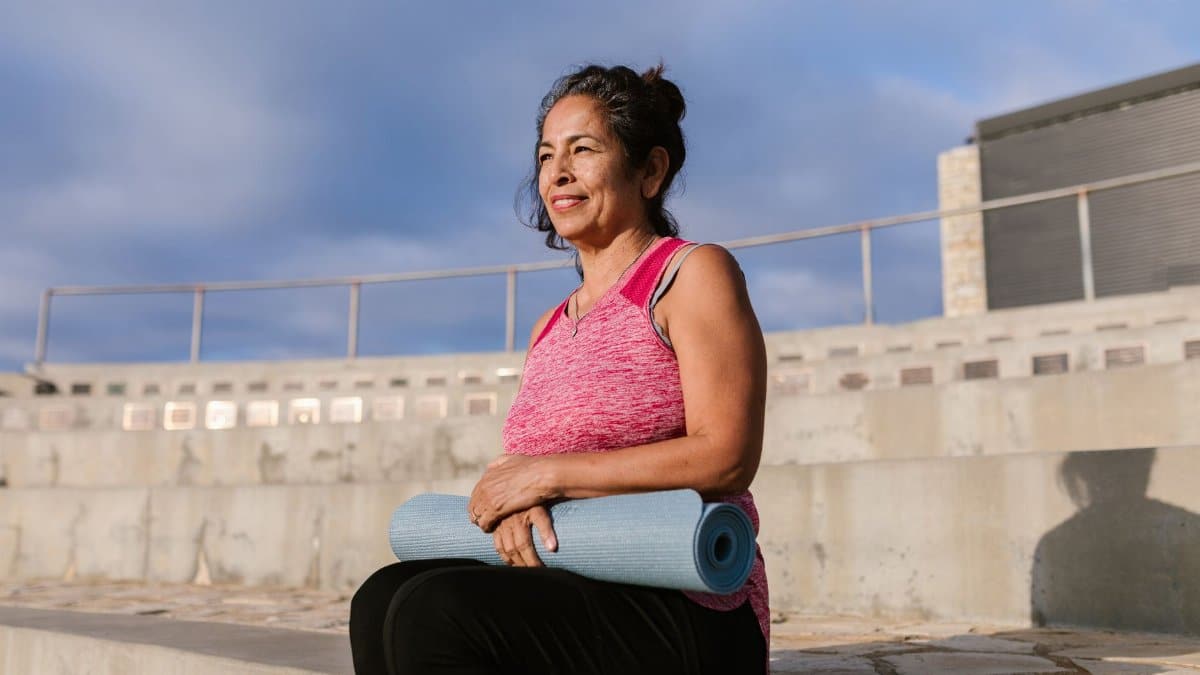 Middle-aged woman holding a yoga mat while enjoying the outdoors. Promotes a healthy lifestyle.