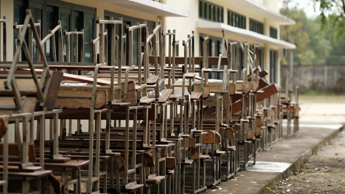A row of stacked old school desks and chairs outside a building.