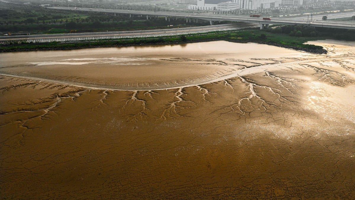 Aerial view of a dry riverbed with a modern bridge in Hangzhou, China, showcasing urban expansion.