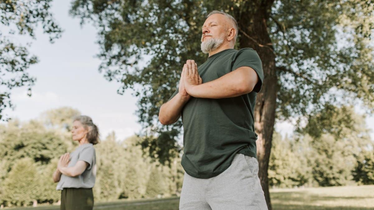 Elderly couple meditating in a peaceful park setting, promoting a healthy lifestyle.