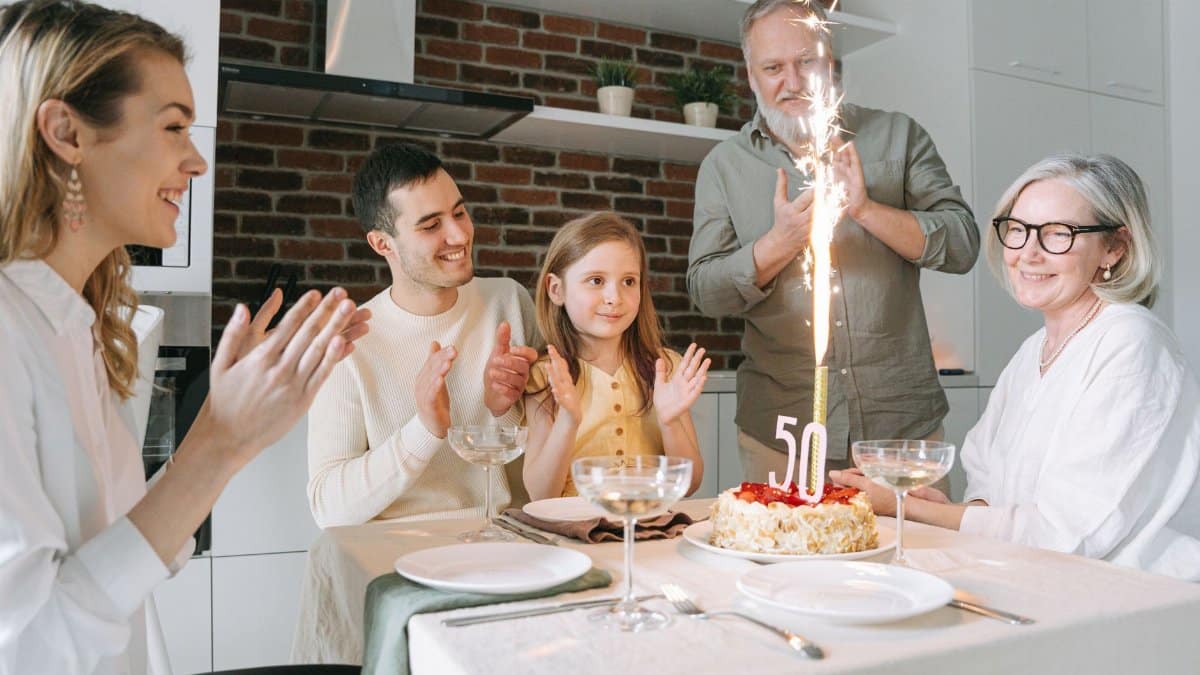 Joyful family gathering around a cake celebrating a 50th birthday indoors.