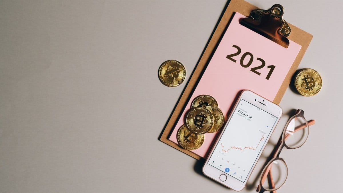 Flat lay of bitcoins, smartphone, eyeglasses, and clipboard with 2021 text, symbolizing cryptocurrency trends.
